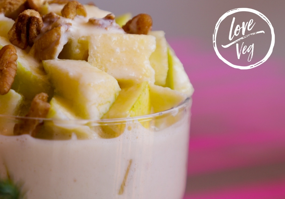 Copa de ensalada dulce de manzana vegana servida en una mesa navideña, con trozos de fruta y crema blanca decorada con nueces.
