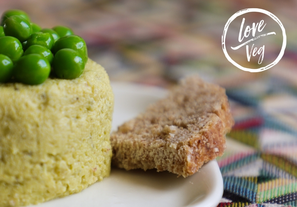 Paté de chícharos en un plato, cubierto con chícharos enteros y rodeado de rebanadas de pan, listo para servir como aperitivo o untable.