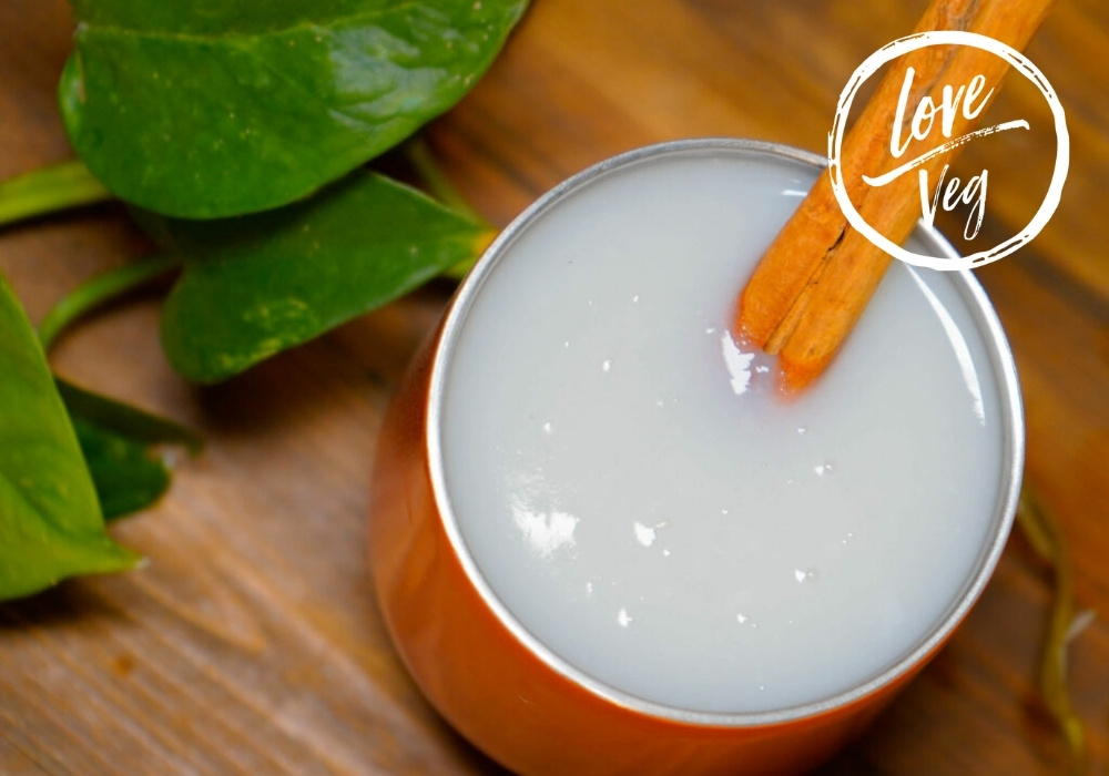 Atole de coco cremoso servido en una taza, con una raja de canela como decoración.