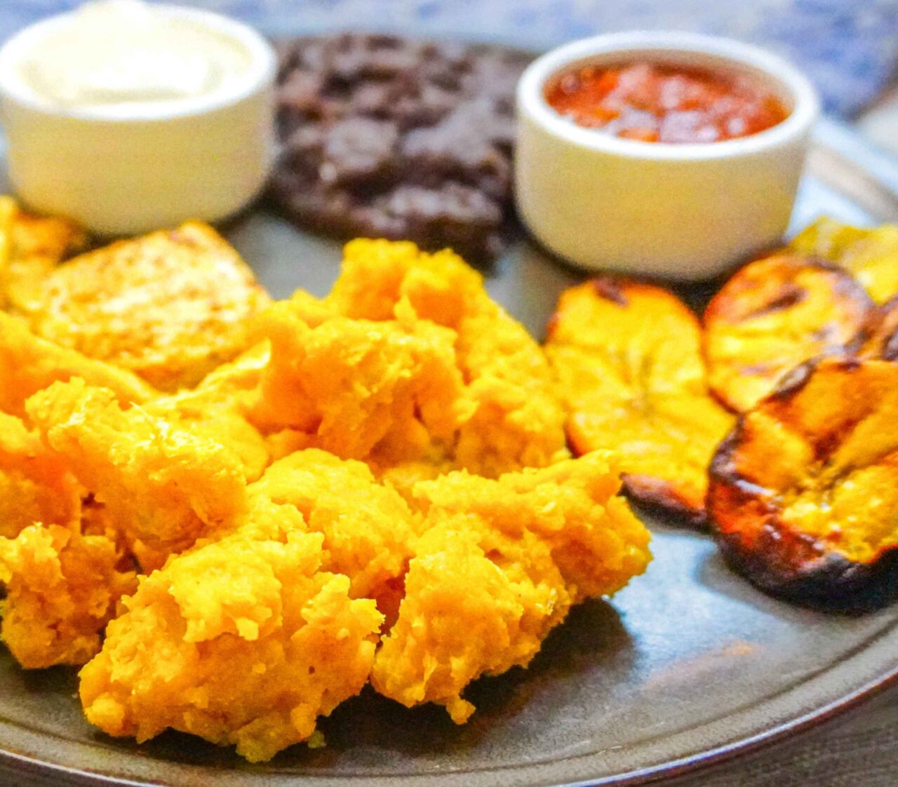 Plato de desayuno chapín vegano con huevo de garbanzo, tofu sazonado tipo queso, crema de tofu, frijoles volteados y plátano maduro asado.