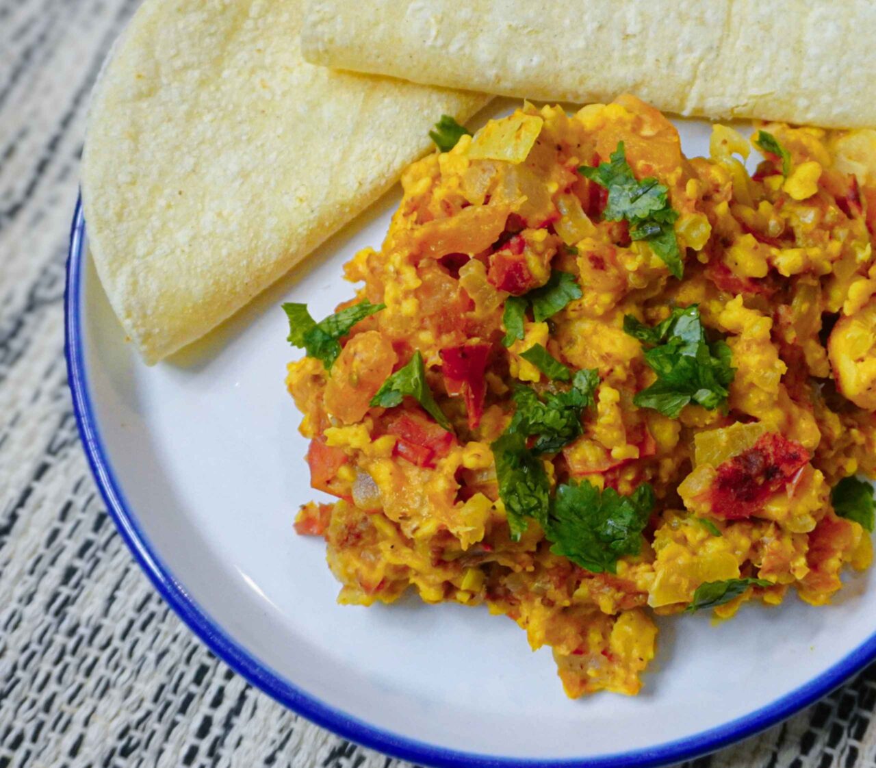 Huevo perico vegano elaborado con harina de garbanzo, mezclado con vegetales salteados y servido en un plato acompañado de tortillas.