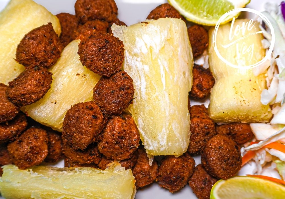 Plato de chicharrón vegano de soya crujiente acompañado de trozos de yuca cocida y una rodaja de limón.