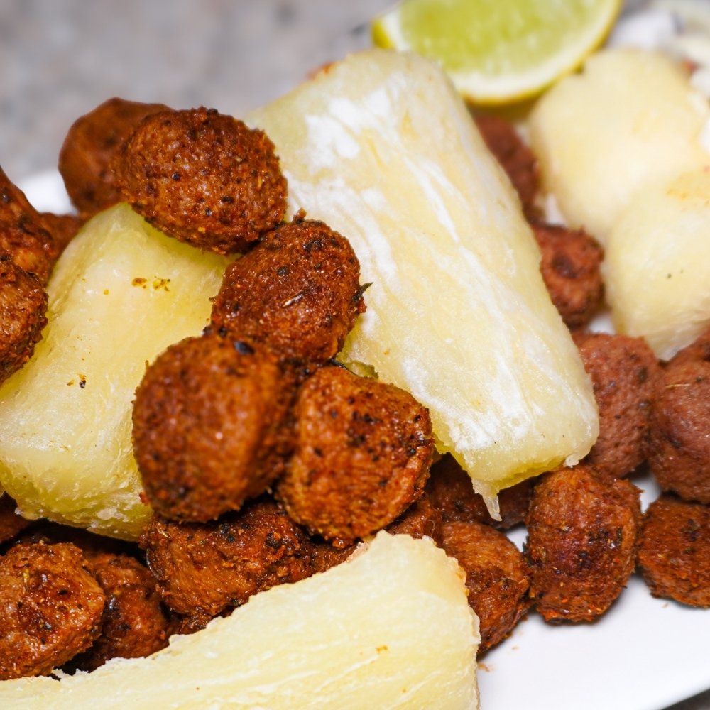 Plato de chicharrón vegano de soya crujiente acompañado de trozos de yuca cocida y una rodaja de limón.