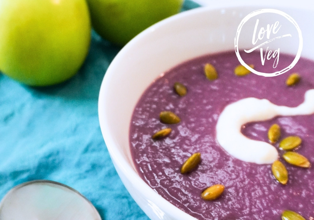 Crema de repollo morado servida en un tazón, de color violeta intenso, decorada con semillas y un toque de crema vegetal.