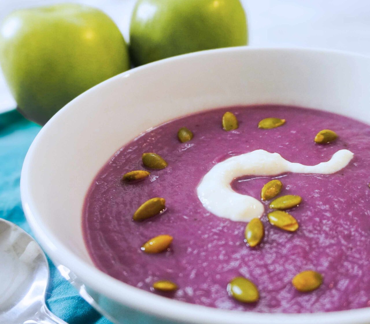 Crema de repollo morado servida en un tazón, de color violeta intenso, decorada con semillas y un toque de crema vegetal.