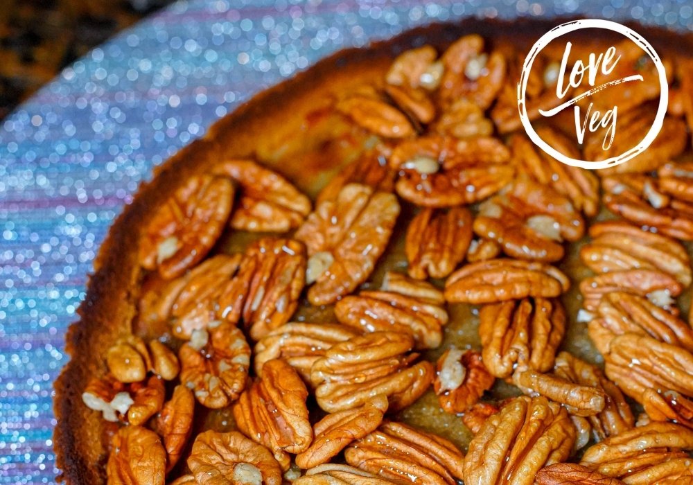 Pie vegano de banana y nueces caramelizadas sobre un plato, con relleno esponjoso y cobertura brillante de nueces enteras.