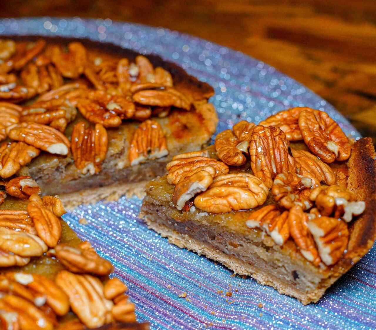 Pie vegano de banana y nueces caramelizadas sobre un plato, con relleno esponjoso y cobertura brillante de nueces enteras.