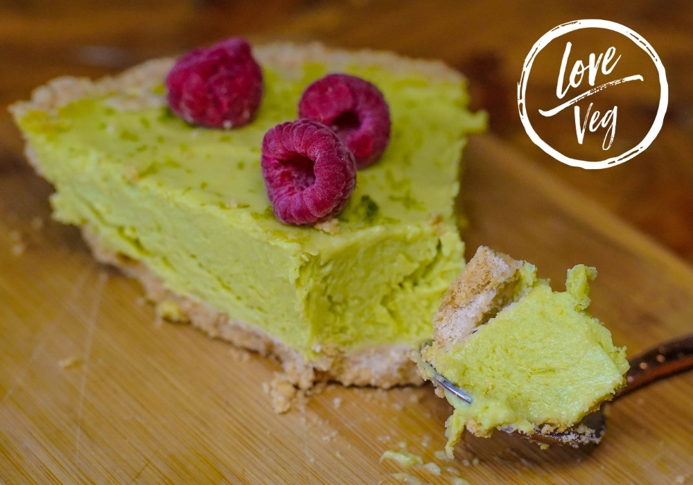 Pie vegano de limón y aguacate sin hornear, decorado con frambuesas mostrando su textura cremosa y color verde claro.