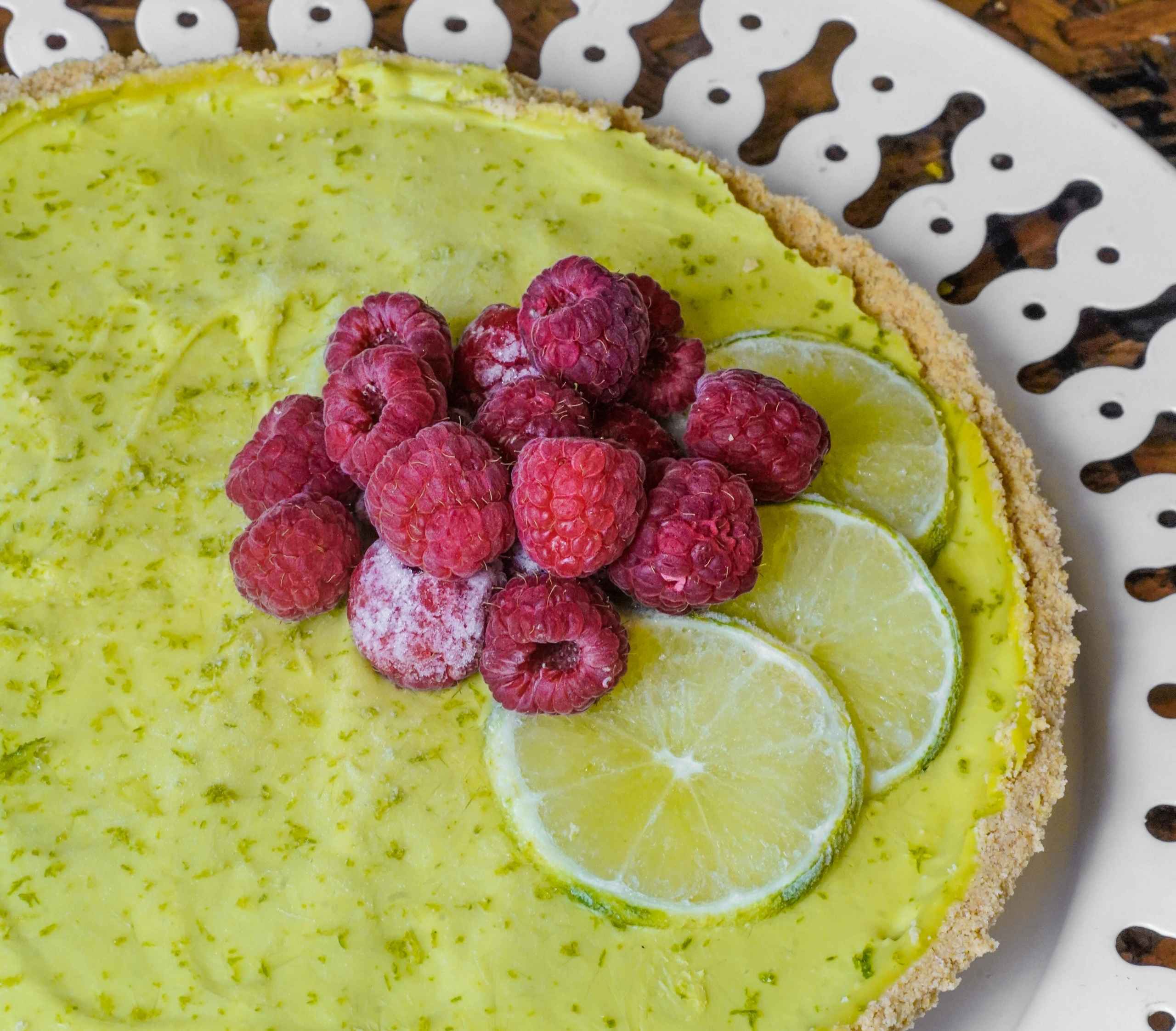 Pie vegano de limón y aguacate sin hornear, decorado con frambuesas mostrando su textura cremosa y color verde claro.