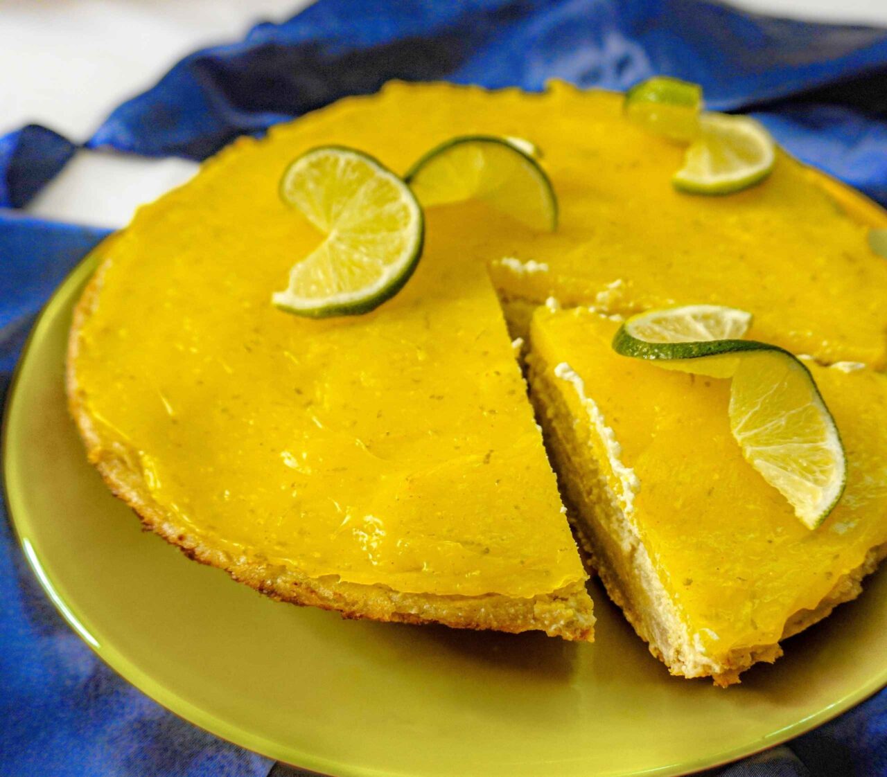 Pie de limón vegano sobre una mesa decorada con mantel y rodajas de limón fresco, con una capa brillante de jalea en la parte superior.