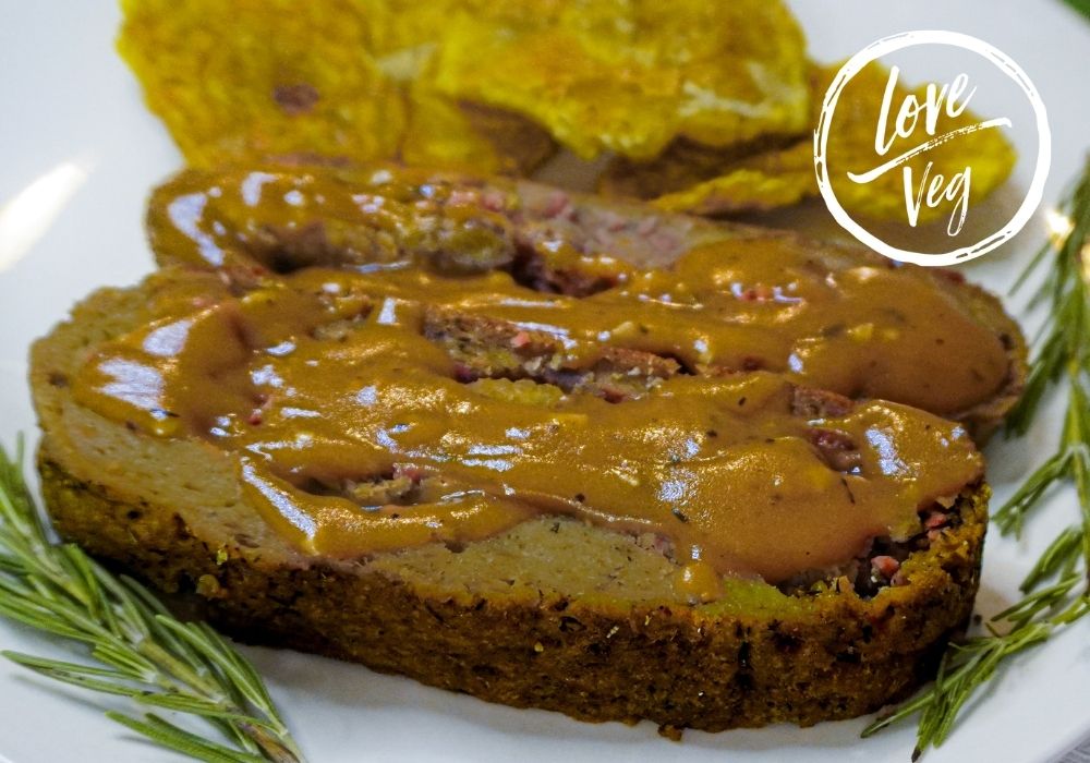 Rollo de pavo vegano hecho con seitan y tofu, relleno de mofongo con bacon bits vegano, servido en un roaster con patacones dorados, listo para la mesa de Thanksgiving.