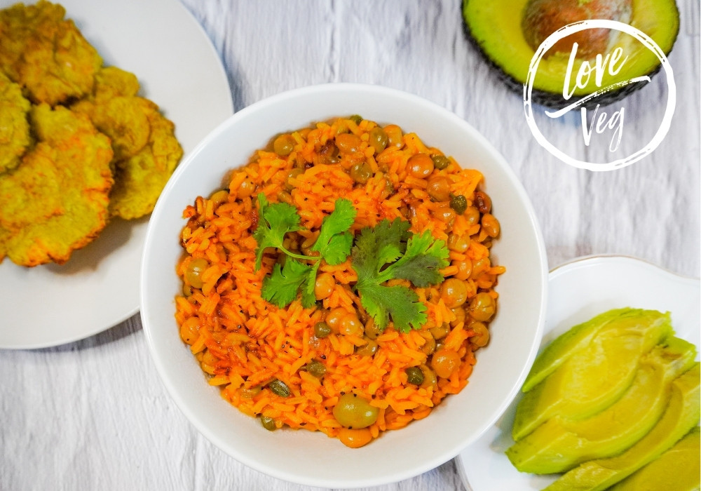 Arroz con gandules vegano servido con patacones crujientes y rodajas de aguacate.