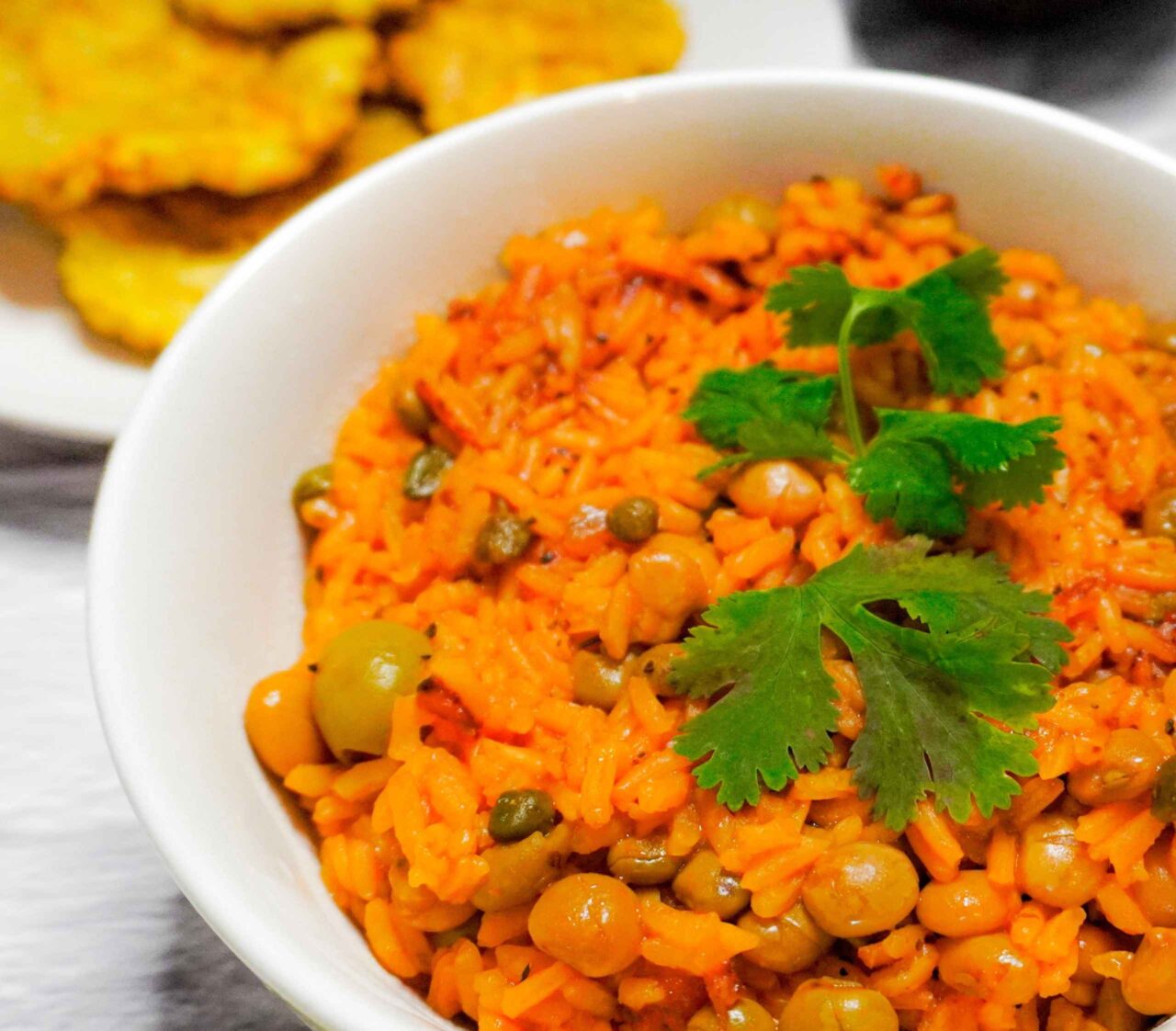 Arroz con gandules vegano servido con patacones crujientes y rodajas de aguacate.