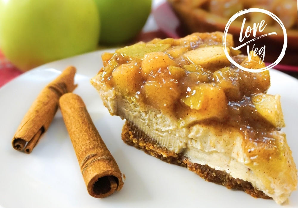 Cheesecake vegano con capa de manzanas caramelizadas con canela y base de galleta graham, servido frío sobre un plato.