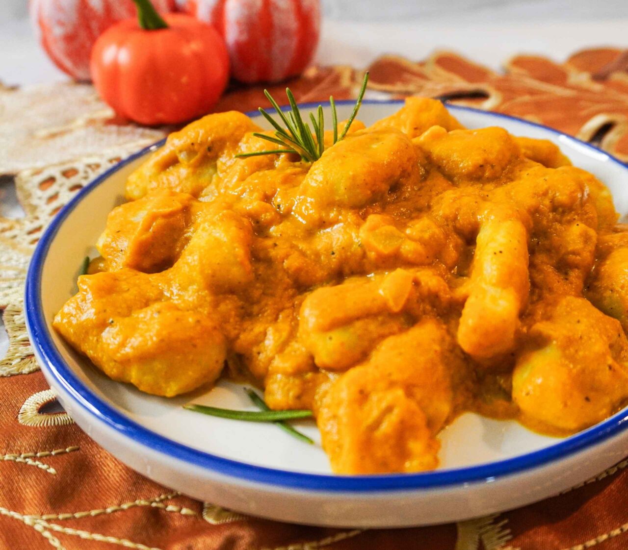 Plato de ñoquis en salsa de calabaza, servidos en un tazón con hojas de romero y pimienta negra, sobre una mesa otoñal.