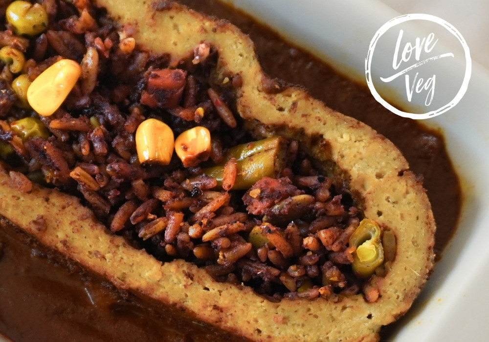 Rollo de pavo vegano de tofu y seitán relleno de arroz con vegetales, servido con mole en una bandeja.