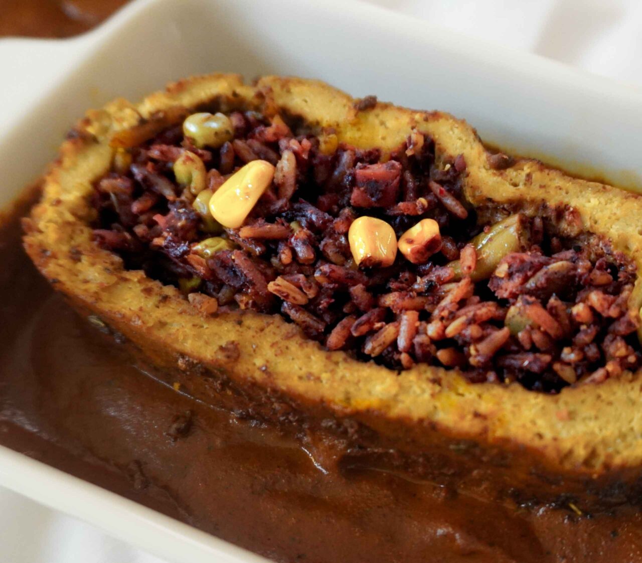 Rollo de pavo vegano de tofu y seitán relleno de arroz con vegetales, servido con mole en una bandeja.
