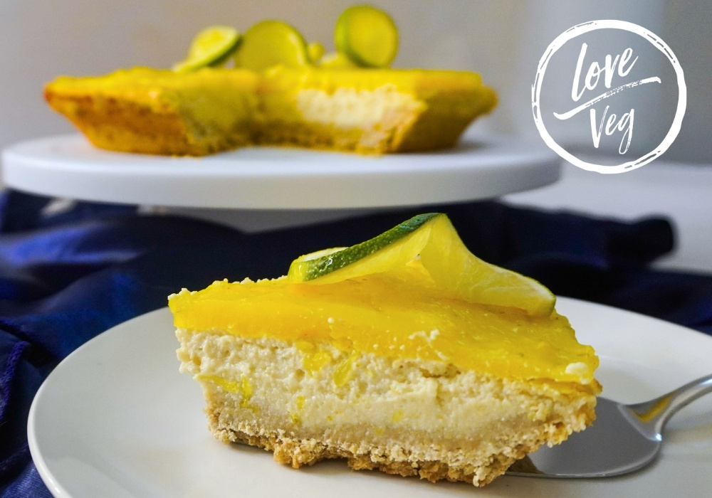 Pie de limón vegano sobre una mesa decorada con mantel y rodajas de limón fresco, con una capa brillante de jalea en la parte superior.