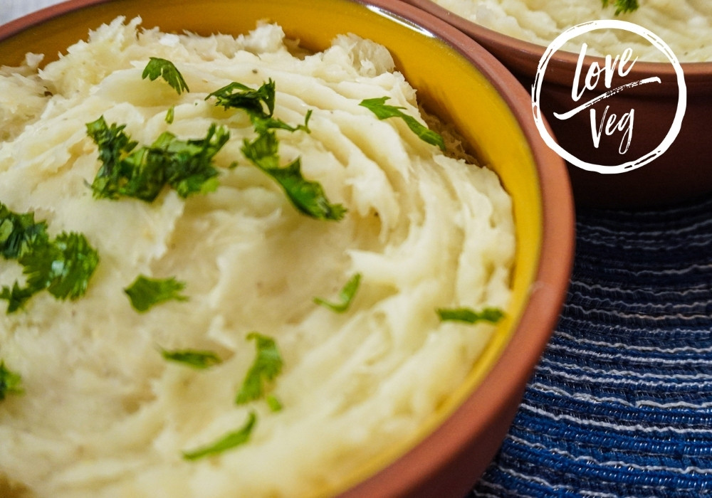 Puré de yuca cremoso servido en un tazón, decorado con hojas de cilantro fresco y un chorrito de aceite de oliva por encima.