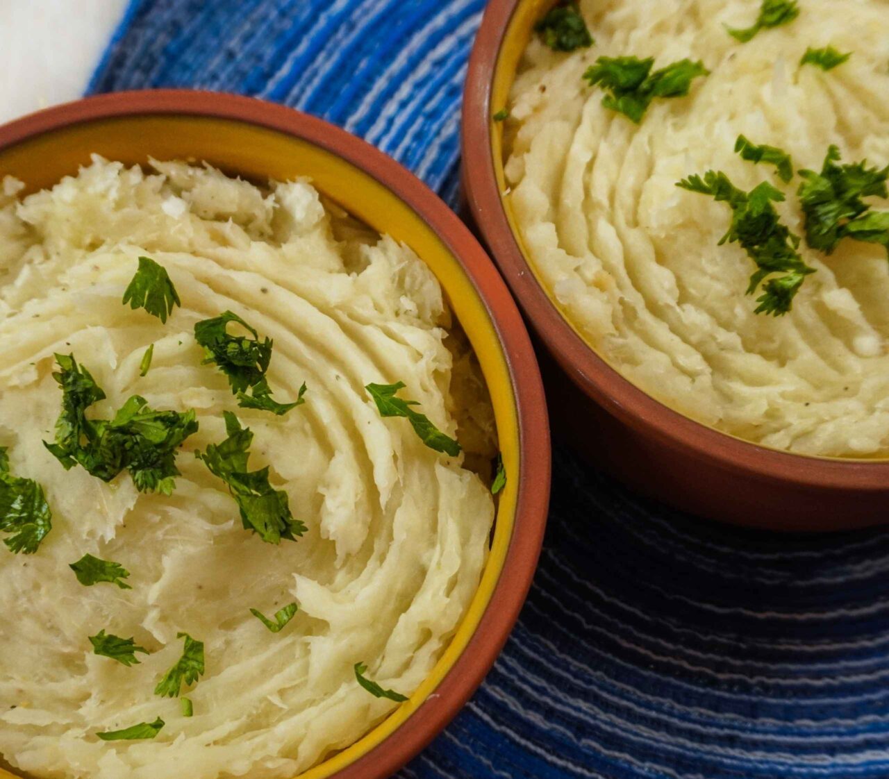 Puré de yuca cremoso servido en un tazón, decorado con hojas de cilantro fresco y un chorrito de aceite de oliva por encima.