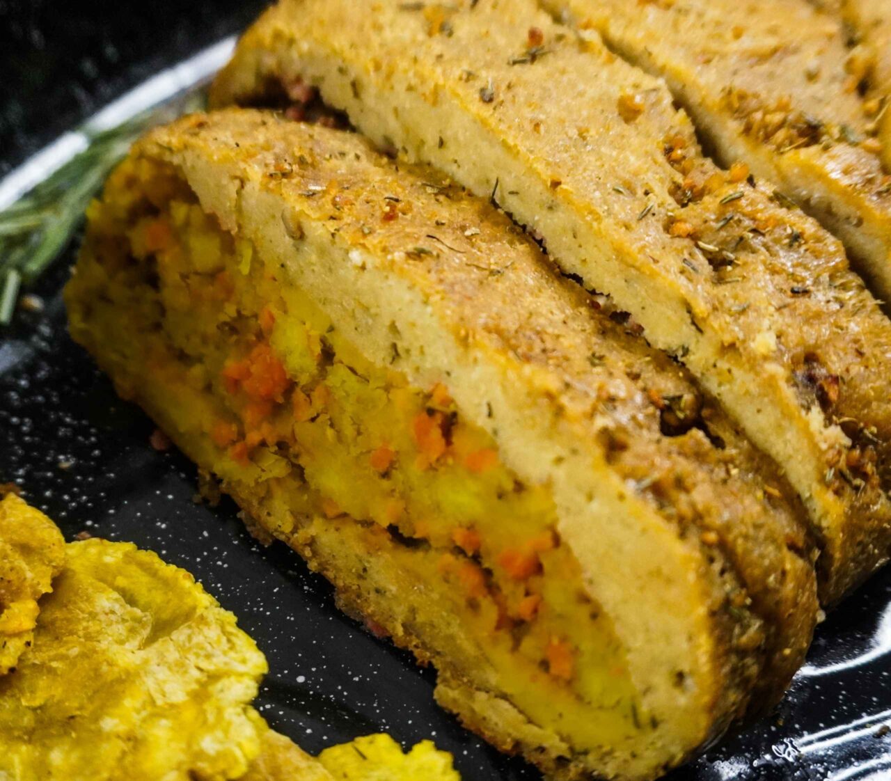 Rollo de pavo vegano hecho con seitan y tofu, relleno de mofongo con bacon bits vegano, servido en un roaster con patacones dorados, listo para la mesa de Thanksgiving.