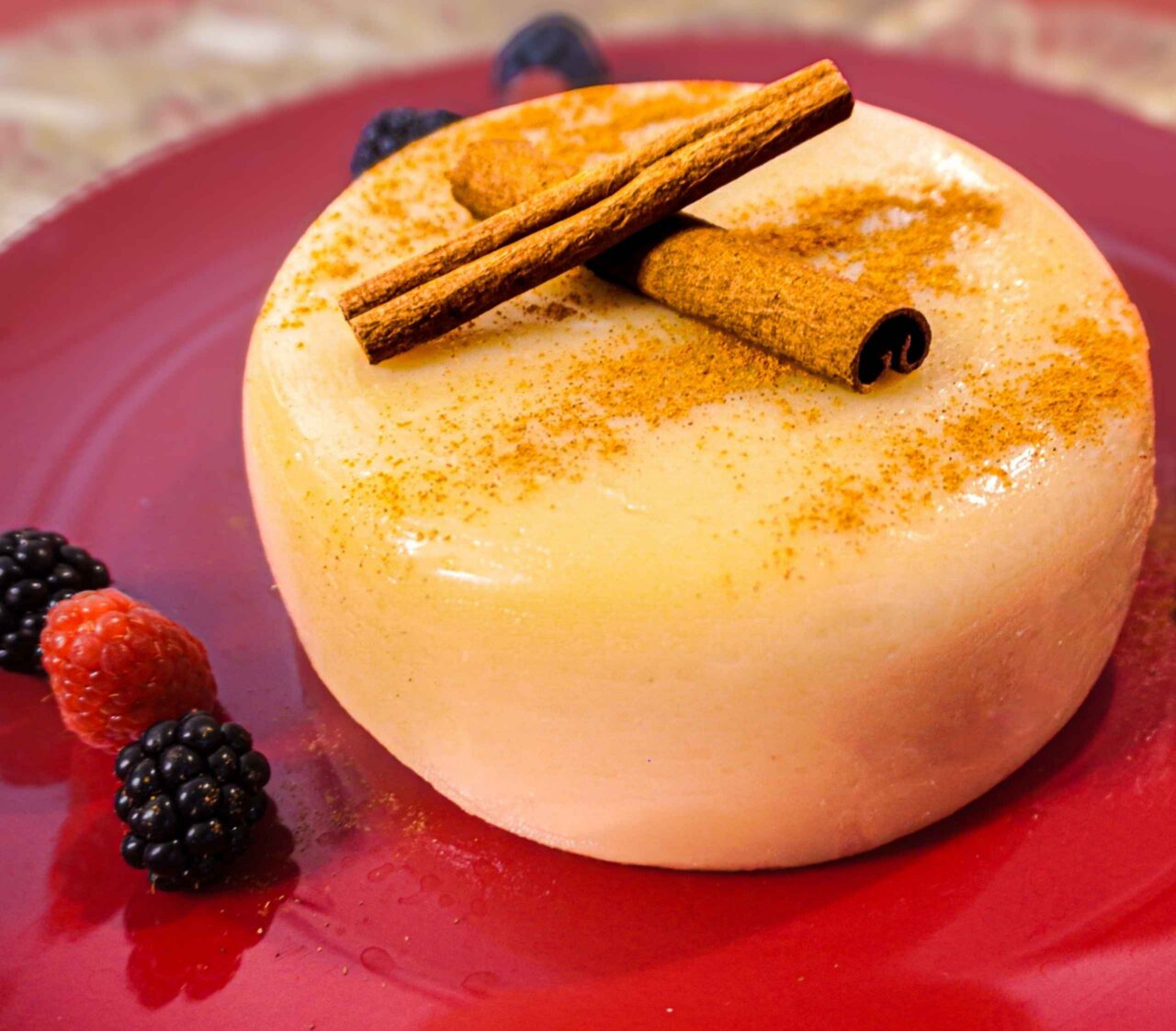 Natilla navideña vegana de color canela servida en un plato blanco, decorada con canela en polvo y una rama de canela.