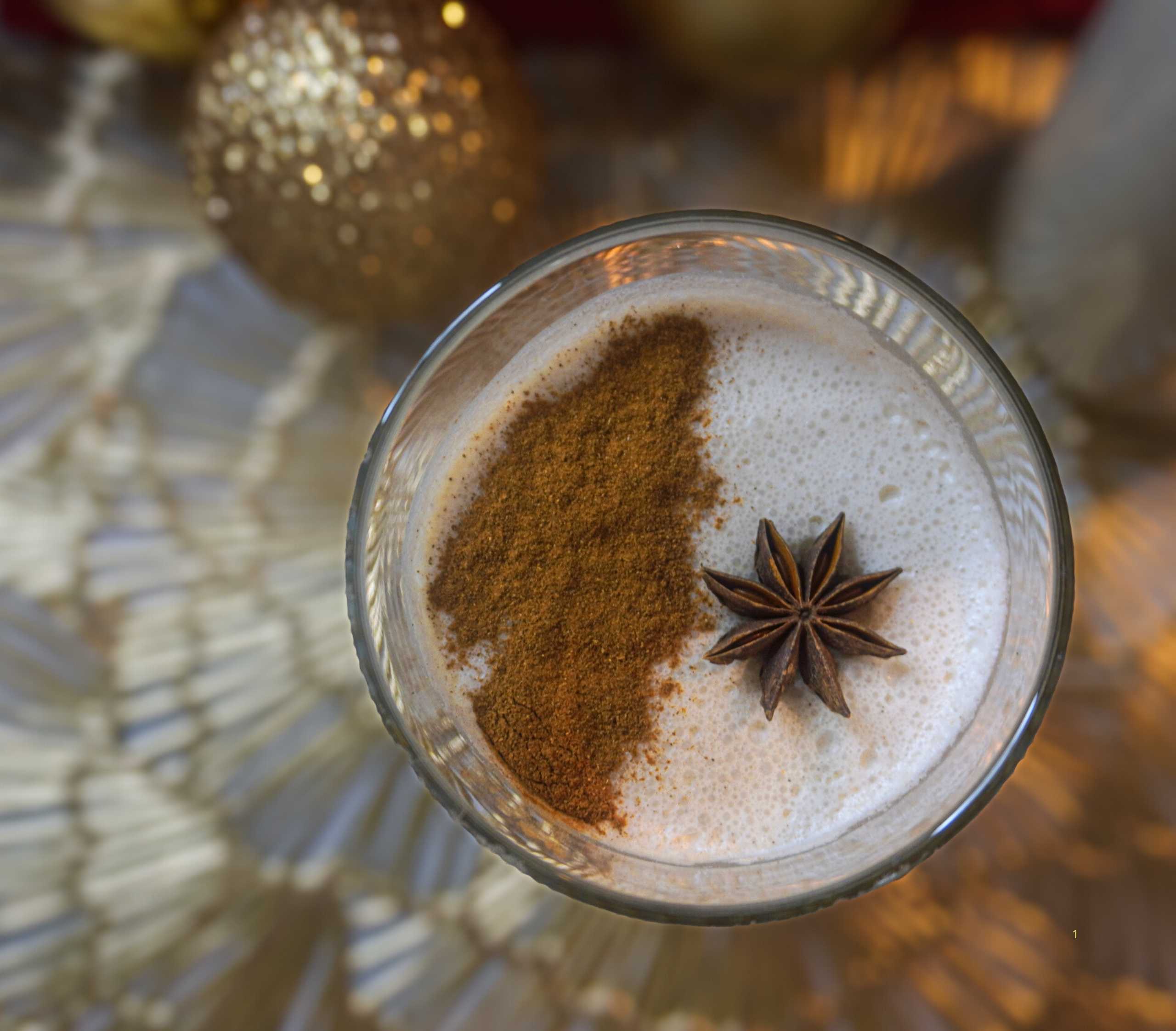 Vaso de coquito vegano sin lácteos, cremoso y decorado con canela en polvo y una ramita de canela.