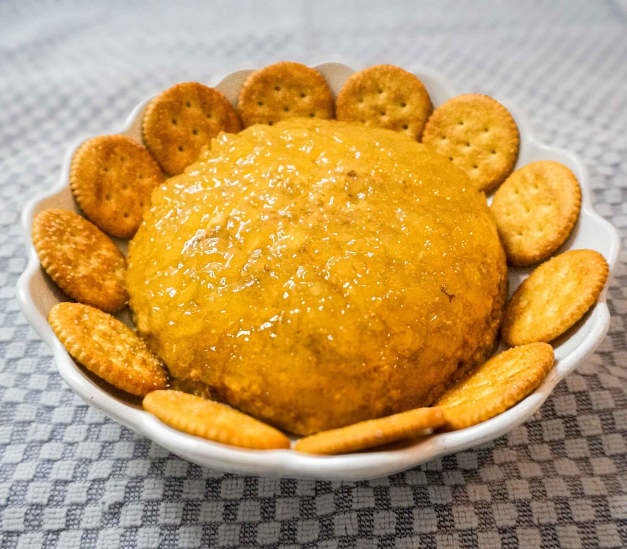 Dip bola de fuego vegano cubierto con una capa dorada, servido en un plato redondo y rodeado de galletas saladas.
