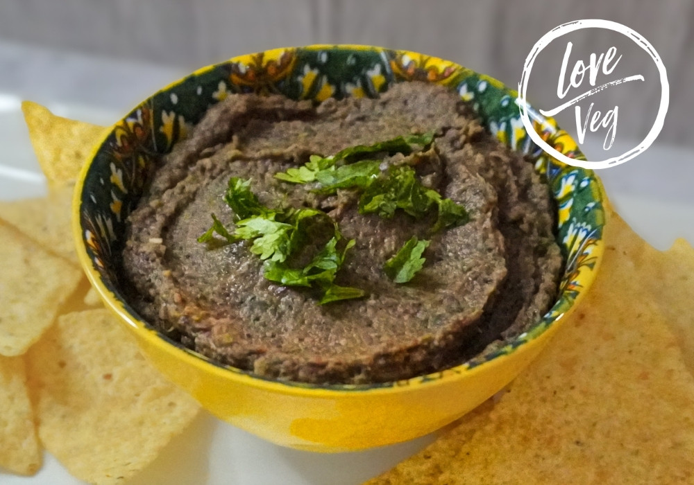 Dip de frijoles negros servido en un tazón amarillo decorado, acompañado de totopos y decorado con cilantro fresco.