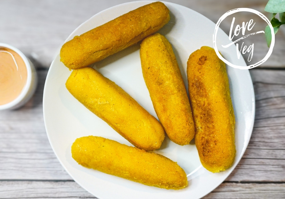 Sorullitos de maíz dorados y crujientes, rellenos de queso de pepitas, servidos en un plato con salsa rosada vegana hecha de ketchup y mayonesa.
