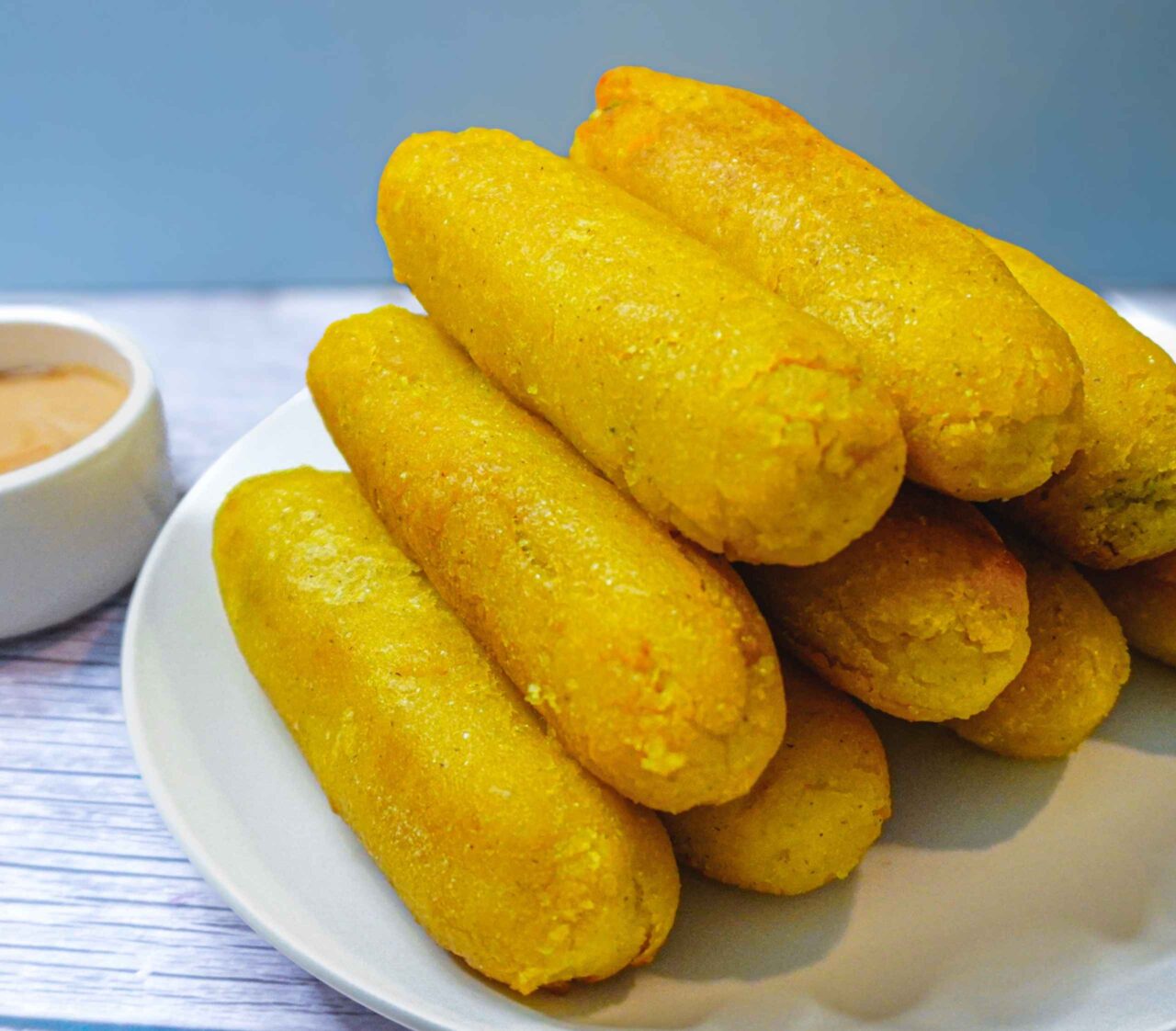 Sorullitos de maíz dorados y crujientes, rellenos de queso de pepitas, servidos en un plato con salsa rosada vegana hecha de ketchup y mayonesa.