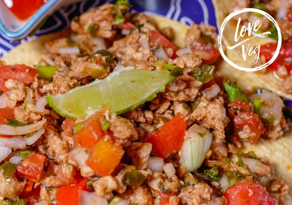 Ceviche vegano de soya texturizada servido sobre tostadas crujientes, con jitomate, cebolla morada, pepino, cilantro y aguacate, decorado con salsa picante y sazonador al gusto.