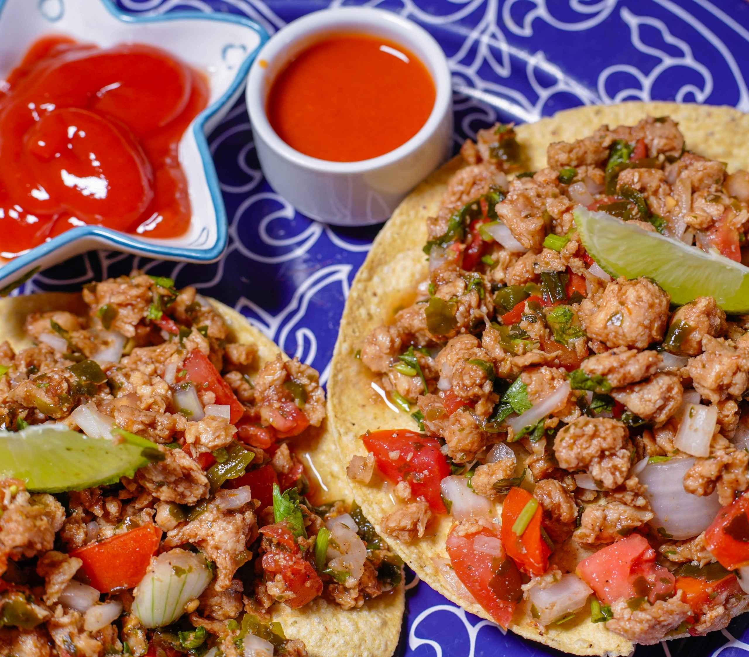 Ceviche vegano de soya texturizada servido sobre tostadas crujientes, con jitomate, cebolla morada, pepino, cilantro y aguacate, decorado con salsa picante y sazonador al gusto.