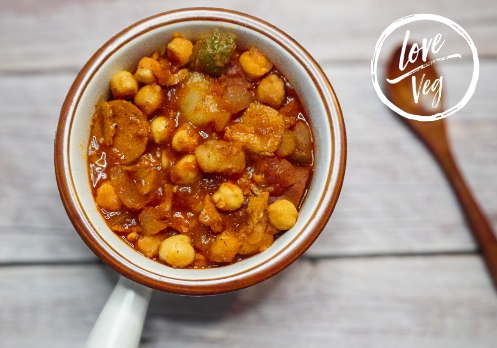 Potaje de garbanzos vegano a la cubana con chorizo y jamón veganos, servido con papas y salsa de tomate.