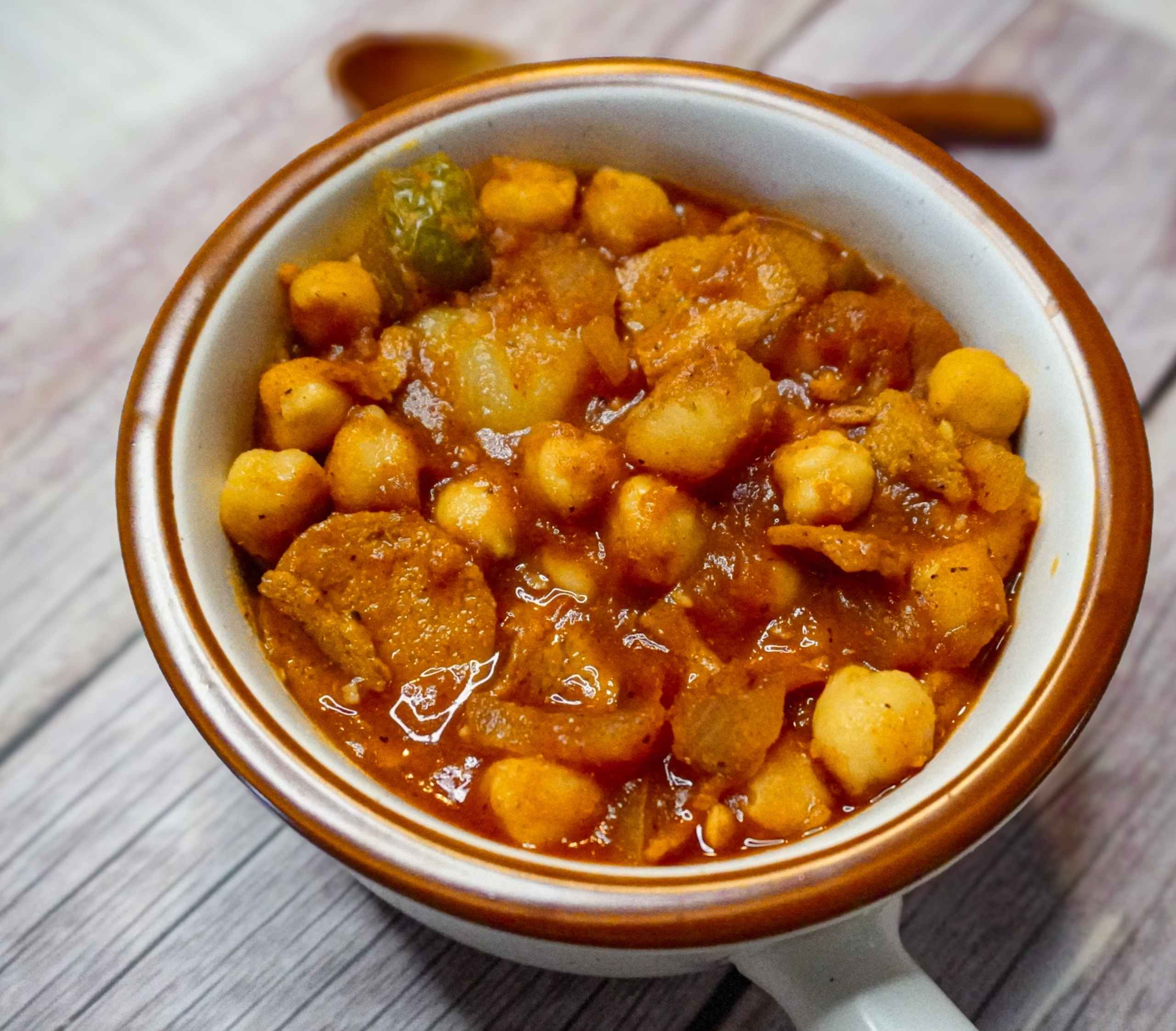 Potaje de garbanzos vegano a la cubana con chorizo y jamón veganos, servido con papas y salsa de tomate.