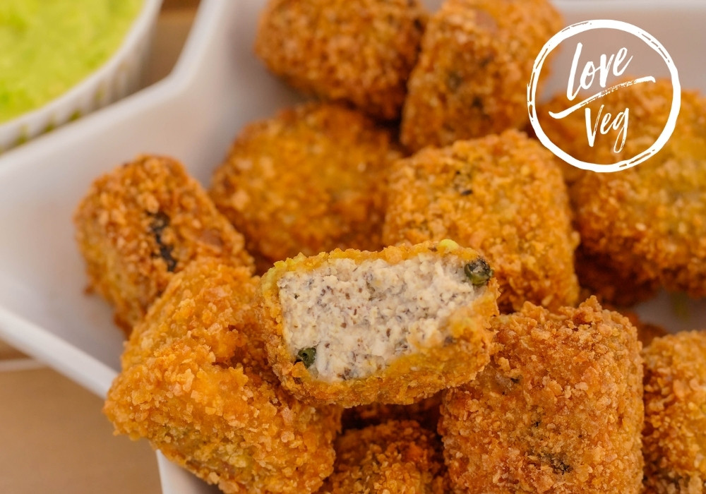 Plato con nuggets veganos de tofu estilo pescado, empanizados y dorados, acompañados de salsa tártara y guacamole, con bebidas cítricas al lado.