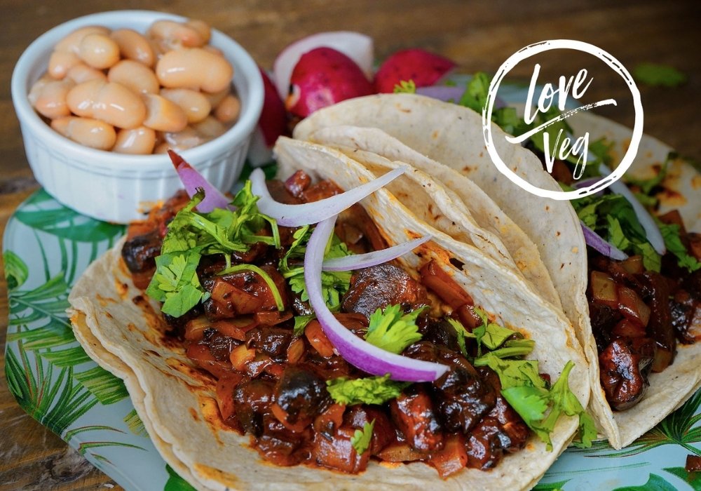 Tacos de hongos adobados con achiote servidos en tortillas de maíz, acompañados de frijoles blancos y guarnición de rábanos.