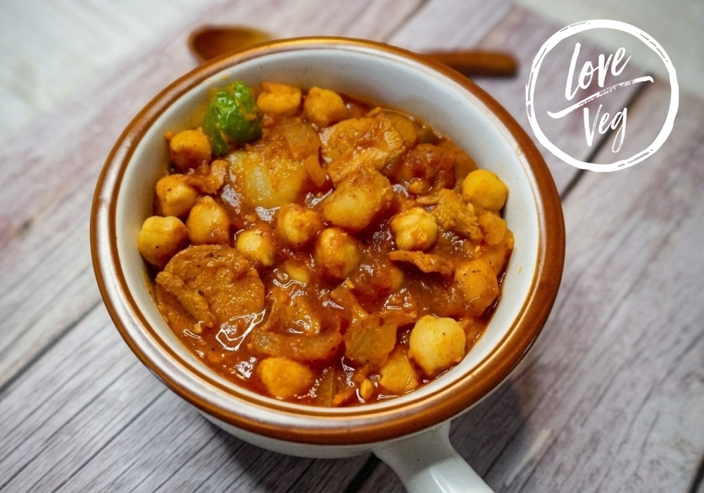 Potaje de garbanzos vegano a la cubana con chorizo y jamón veganos, servido con papas y salsa de tomate.