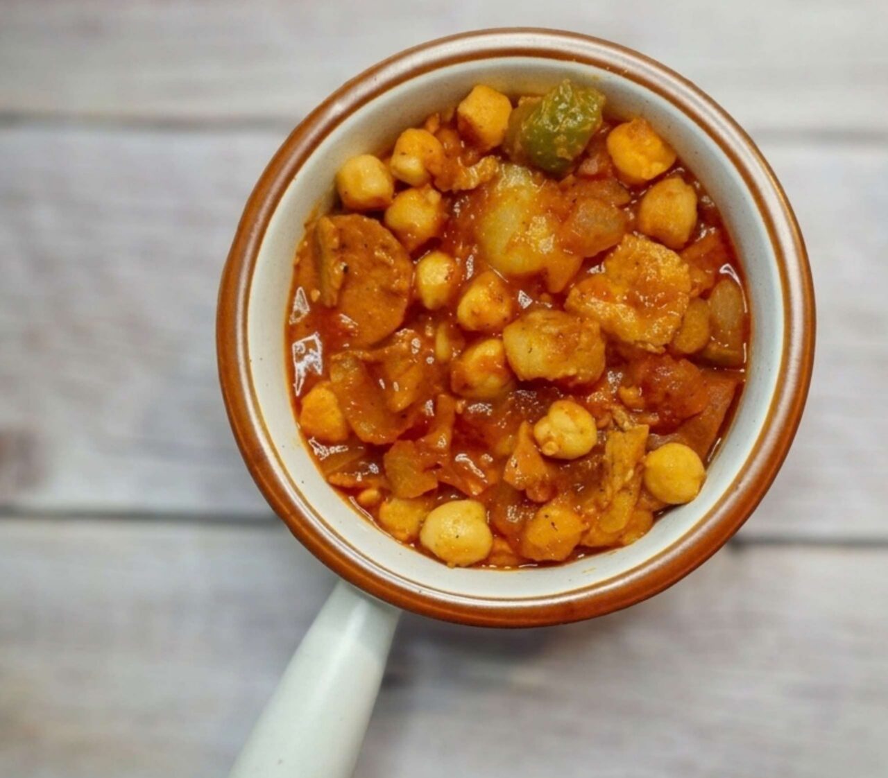 Potaje de garbanzos vegano a la cubana con chorizo y jamón veganos, servido con papas y salsa de tomate.