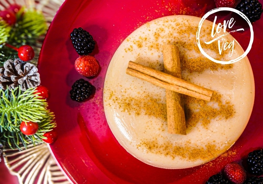 Natilla navideña vegana de color canela servida en un plato blanco, decorada con canela en polvo y una rama de canela.