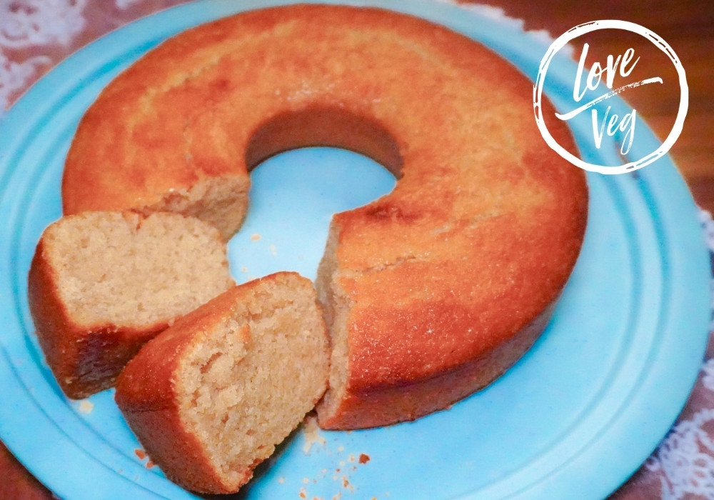 Queque seco vegano de naranja y vainilla con textura esponjosa y miga porosa, servido en un plato azul. Receta de repostería basada en plantas con aquafaba.