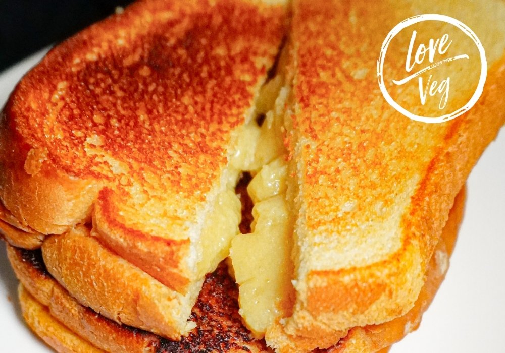 Sándwich de queso vegano derretido hecho con leche de avena y pan tostado dorado en una sartén.